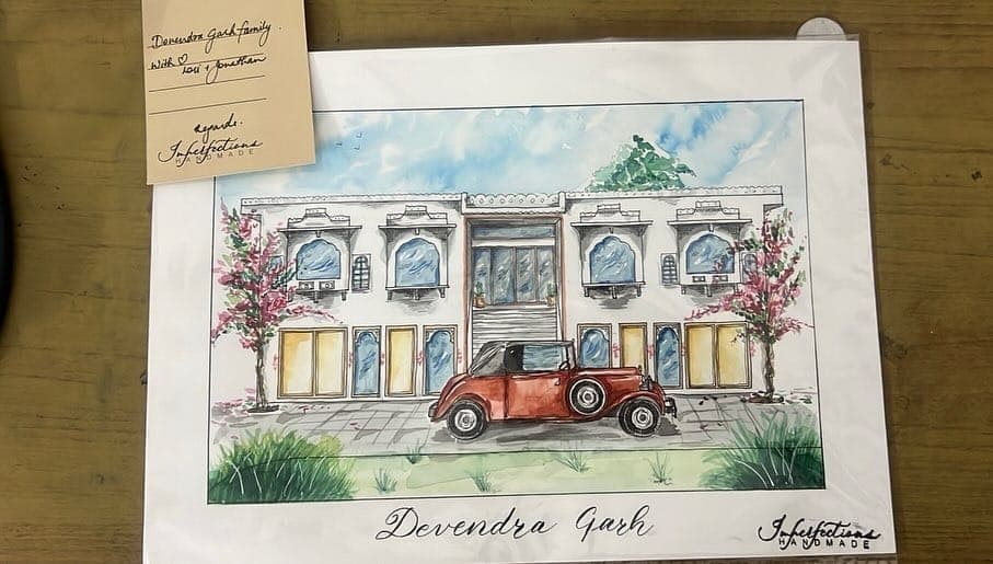 The watercolour of the haveli lying on a wooden table with a handwritten note card resting on its top left corner