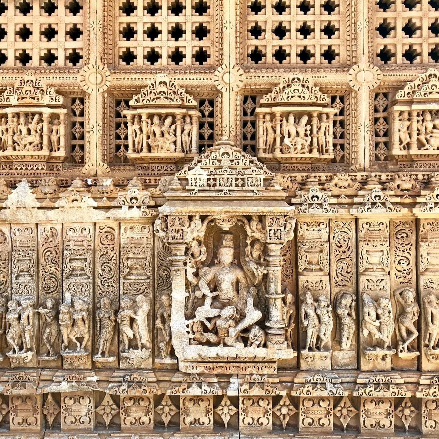 A sandstone temple wall carved in tiered bands of standing figures, dancers and pierced lattice screens